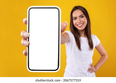 App Ad. Smiling pretty woman holding smartphone with white blank device screen in hand close up to camera, orange studio. Gadget with empty free space for mockup, banner isolated, selective focus - Shutterstock ID 2067577319
