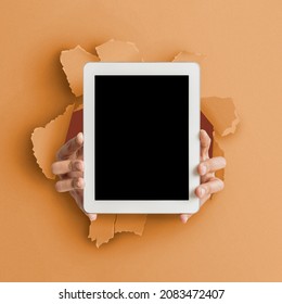 App Advert, Great Offer. Closeup Of Person Holding Tab With Empty Screen In Hands Showing Device Close To Camera Breaking Through Orange Paper Sheet Hole. Gadget Display With Free Copy Space, Mock Up