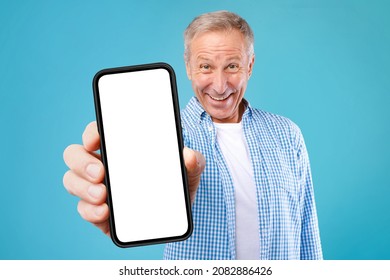 App Advertisement. Excited Mature Man Showing Big White Empty Smartphone Screen Recommending Website Posing Over Blue Studio Background, Smiling To Camera. Check This Out, Cellphone Display Mock Up