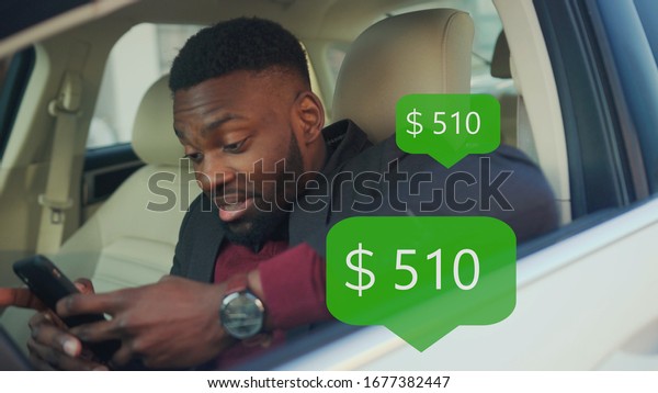 App Icon with Online Transaction. Financial
Transactions in the Smartphone. Receive a Message About Increase
Money. Happy African American Young Businessman Use Phone In A Car
Smile Sits Behind The
