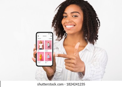 App For Online Store. Happy african woman holding and showing phone with clothes shop website and pointing at screen