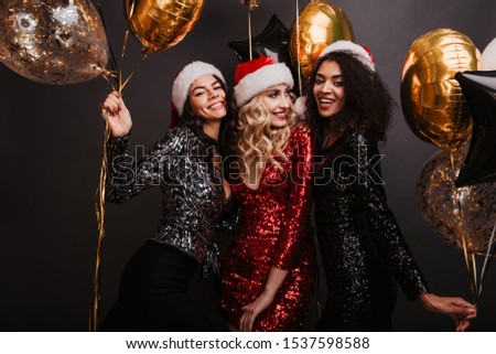 Appealing blonde woman in red dress celebrating winter holidays with friends. Studio shot of girls dancing with balloons.