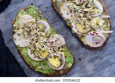 Appetising healthy breakfast. Two slices of avocado toast on a homemade sourdough brown bread with sliced eggs, mungo bean sprouts, fresh pepper and chilli flakes