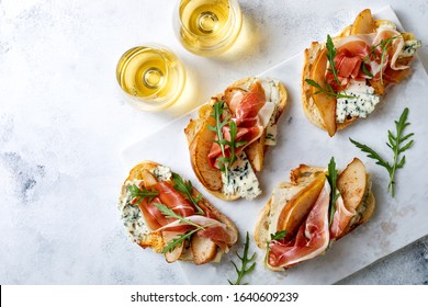 Appetitzüge Crostini, Tapas, offene Sandwiches mit Birne, Prosciutto, Arugula und blauer Käse auf weißem Marmorbrett. Köstliche Snacks, Vorspeisen