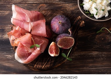 Appetizer from dry cured ham, prosciutto slices with figs on a dark wooden background, rustic style.
