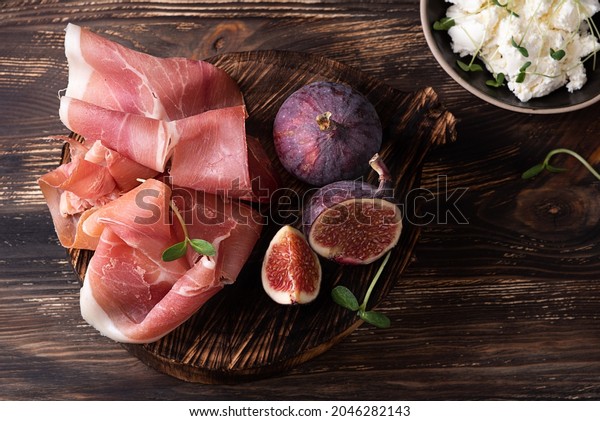 Appetizer from dry cured ham,\
prosciutto slices with figs on a dark wooden background, rustic\
style.