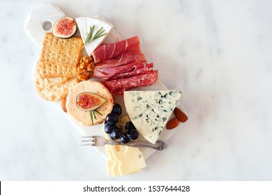 Appetizer Platter With Assorted Cheeses And Cold Cut Meats. Top View On A White Marble Background.