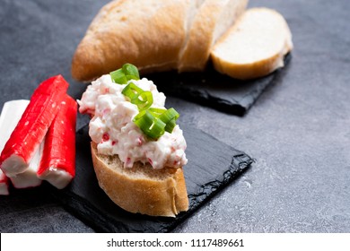 Appetizer with surimi sticks and mayonnaise served on a black slate tray. 