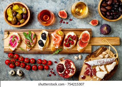 Appetizers table with italian antipasti snacks and wine in glasses. Brushetta or authentic traditional spanish tapas set, cheese variety board over grey concrete background. Top view, flat lay - Shutterstock ID 754215307