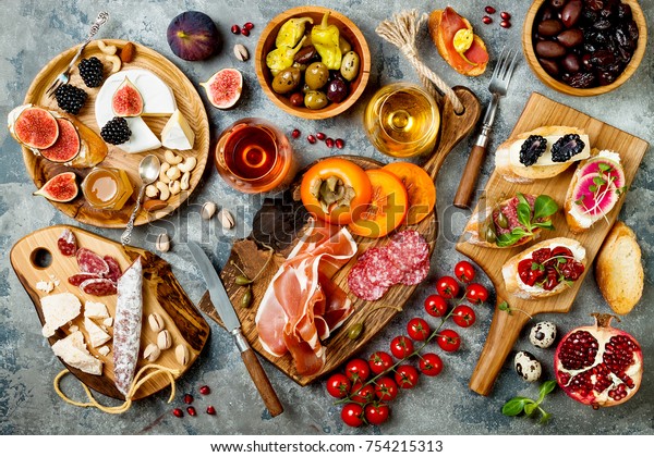 Appetizers table with italian antipasti snacks and\
wine in glasses. Brushetta or authentic traditional spanish tapas\
set, cheese variety board over grey concrete background. Top view,\
flat lay