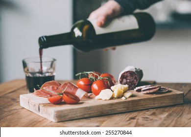 Appetizers - tomato, meat and cheese - on wooden board with bottle of wine and glass. Toned image - Powered by Shutterstock