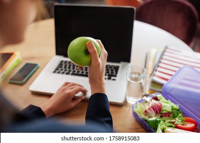 Appetizing apple. Green juicy apple in female hands over a table with a laptop and a lunchbox with vegetables.