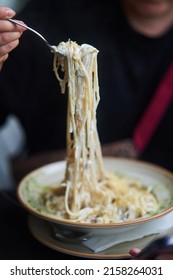 Appetizing carbonara paste with chicken improperly wound on fork. Spaghetti inaccurately hanging and falling from fork. Close up.