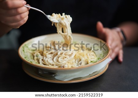Appetizing carbonara paste with chicken improperly wound on fork. Spaghetti inaccurately hanging and falling from fork. Close up. High quality photo