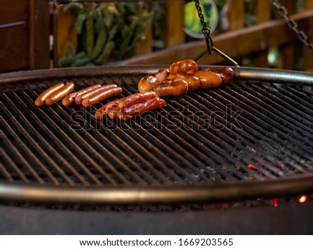 Appetizing delicious sausages lie on the grill of a roasting pan in the dark.  From underneath the grill, hot coals burn.  Outdoor festive refreshments in the city.