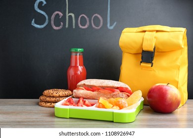 Appetizing Food In Lunch Box And Bag On Table Near Chalkboard With Word SCHOOL