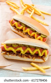 Appetizing French Fries And Hot Dogs With Mustard And Grilled Onions, Close-up. Baking Paper, Wooden Background. Couch Potato Food.