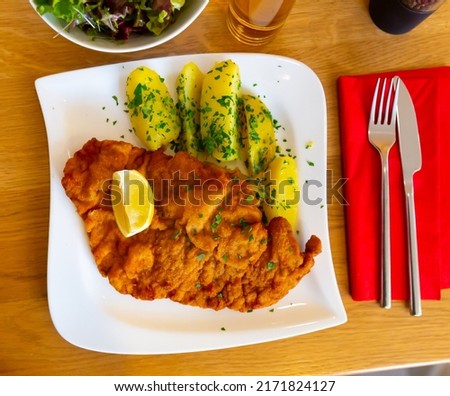 Appetizing fried fish filet in crispy breading with lemon slice served with side dish of boiled potatoes with greens and fresh vegetable salad. Traditional Turkish cuisine