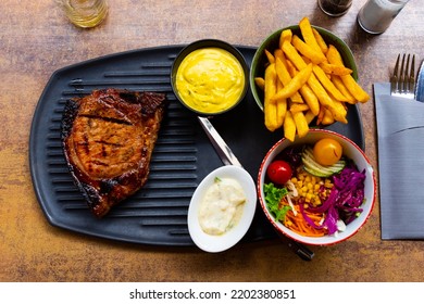 Appetizing grilled pork loin chop brined in beer according to old Belgian recipe, served with french fries, salad and sauce