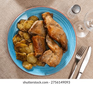 Appetizing roasted rabbit pieces with vegetable garnish of fried potatoes. Delicious and satisfying homemade dinner..