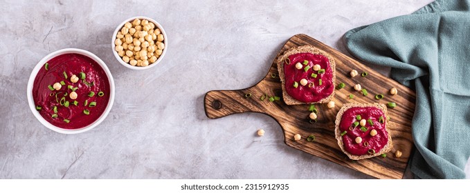 Appetizing rye bread bruschettas with beetroot hummus and chives on a cutting board top view web banner