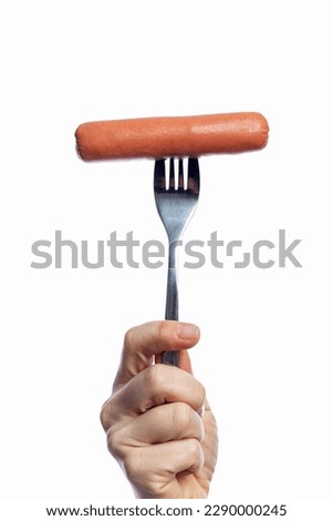 Appetizing sausage on a fork in a woman's hand. Traditional fast food. Isolated on a white background. Close-up. Vertical.