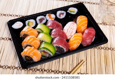 Appetizing set of nigiri sushi, uramaki and norimaki rolls with salmon, tuna, shrimp and avocado served in black plastic tray. Japanese cuisine. Delivery or takeaway food concept - Powered by Shutterstock