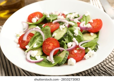 Appetizing spinach salad with cheese, walnuts and vegetables on table, closeup