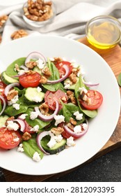 Appetizing spinach salad with cheese, walnuts and vegetables served on black table, closeup