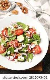Appetizing spinach salad with cheese, walnuts and vegetables served on black table, closeup