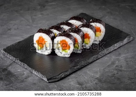 appetizing sushi roll futomaki with cucumber and salmon on a black stone plate.