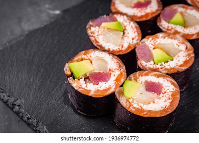 appetizing sushi rolls with tuna salmon escolar crab and avocado on a black stone plate.