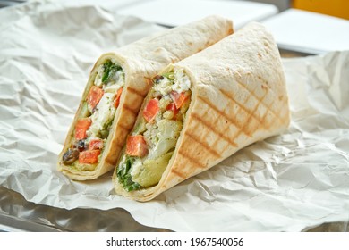 Appetizing vegetarian doner roll with vegetables, sauce and pesto sauce in pita bread, served on paper on a light background. Traditional street food - shawarma - Powered by Shutterstock