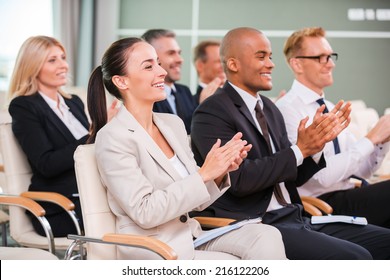 Applauding to speaker. Group of happy business people in formalwear sitting at the chairs in conference hall and applauding 