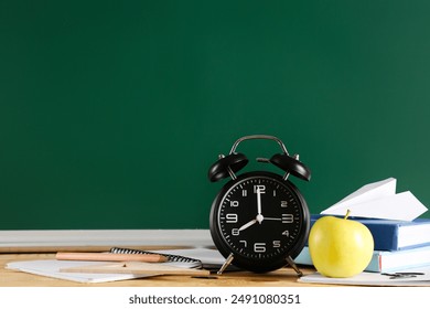 Apple, alarm clock, books and paper plane on desk near chalkboard. Back to school concept - Powered by Shutterstock