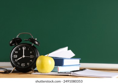 Apple, alarm clock, books and paper plane on desk near chalkboard. Back to school concept - Powered by Shutterstock