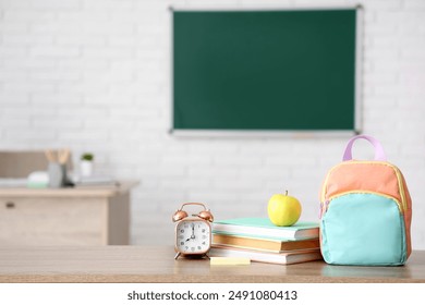 Apple, alarm clock, books and schoolbag on desk in classroom. Back to school concept - Powered by Shutterstock