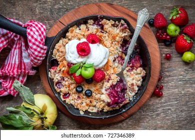 Apple and berry crumble with oats on rustic wooden background, autumn dish, healthy breakast concept