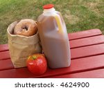 apple cider, an apple and a bag of cinnamon-sugared donuts on a red picnic table