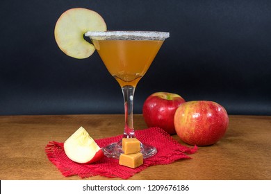 apple cider martini with caramel apples and ripe apples on wood table