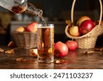 Apple cider is poured from a bottle into a glass. Fresh drink with apples on an old kitchen table.