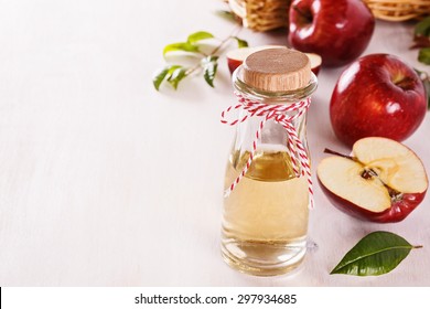 Apple cider vinegar and red apples over white wooden background with copyspace. Selective focus