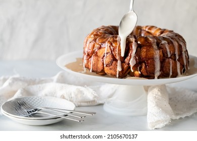 Apple cinnamon monkey bread on a pedestal stand with icing being drizzled on top - Shutterstock ID 2105670137
