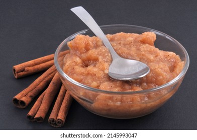 Apple With Cinnamon Sticks And A Ramekin Of Compote Close-up On A Black Background