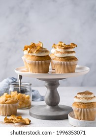 Apple cupcakes with cream cheese frosting decorated with dried apple slices and cinnamon powder. Autumn festive dessert. Homemade tasty pastry on ceramic cake plate. Close up food.