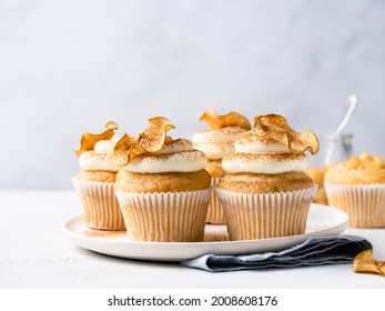 Apple cupcakes with cream cheese frosting decorated with dried apple slices and cinnamon powder. Autumn festive dessert. Homemade pastry on ceramic plate. Close up food. Copy space. Morning table.