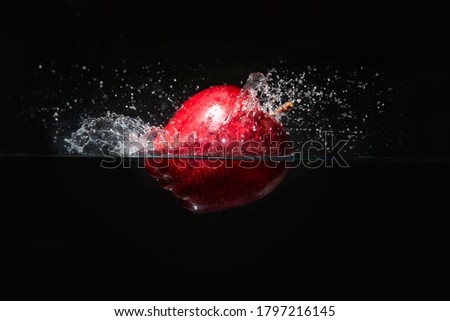 Apple falling in water isolated on black background.