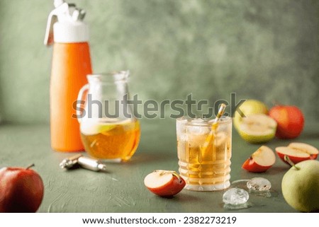 Apple juice and sparkling water in glass. Apfelschorle German drink. Apple fruit, ice and leaves in background. Summertime cold drink