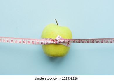 Apple with measuring tape on blue background. Weight loss, counting calories and healthy eating concept - calculate daily nutrition intake. Top view. Copy space.