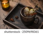 Apple Moscow Mule cocktail in a copper mug on a wooden rustic background. Autumnal Spiced Cider with honey, apple slices, thyme and cinnamon stick as a garnish. Cozy autumn evening. Drink photography